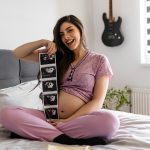 Donna incinta in pigiama che mostra felicemente le prime ecografie del nascituro, dopo avere superato i sintomi della gravidanza dei primi giorni