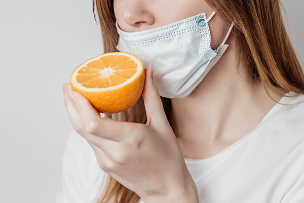 Donna che indossa una mascherina medica e non riesce a sentire l’odore dell’arancia, mentre si interroga sulle cause dell’anosmia