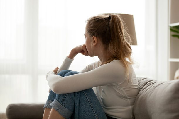 donna-seduta-sul-divano-con-nervosismo Giovane donna seduta sul divano di casa, mentre guarda fuori dalla finestra per fare passare il suo sentimento di nervosismo