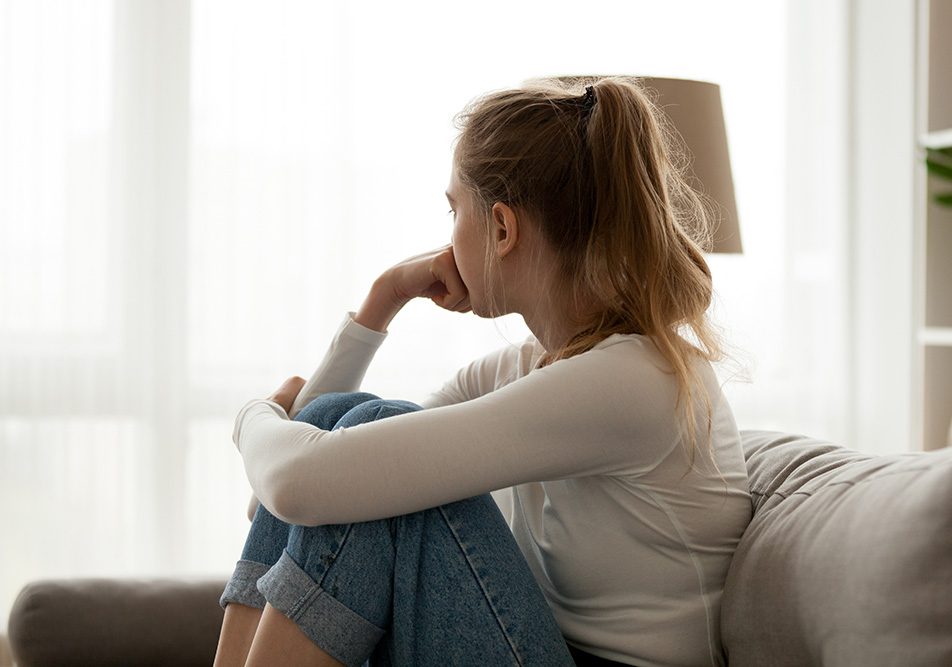 donna-seduta-sul-divano-con-nervosismo Giovane donna seduta sul divano di casa, mentre guarda fuori dalla finestra per fare passare il suo sentimento di nervosismo