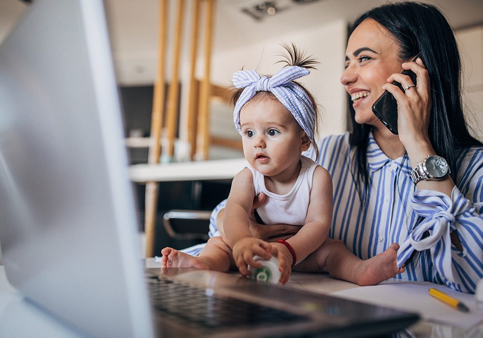 Mamma e bambina che lavorano assieme alla scrivania lavanti al PC; il genitore è al telefono per domandare informazioni sul bonus mamme lavoratrici