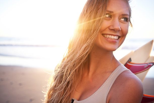 ragazza-surfando-in-spiaggia-dopo-protezione-capelli-sole Ragazza dalla chioma bionda che surfa in spiaggia al tramonto, dopo avere applicato una protezione dei capelli dal sole