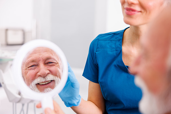 Signore che osserva il suo sorriso curato dalla dentista, che gli ha riparato una carie radicolare