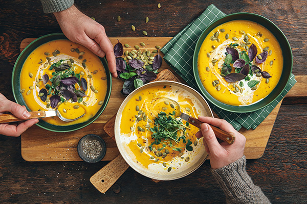 Uomini al tavolo che consumano una zuppa di zucca con semi e germogli vari, cibi autunnali nutrienti e sani