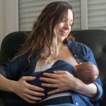 donna seduta in poltrona allatta al seno neonato