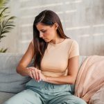 donna seduta sul divano guarda braccio con dermatite