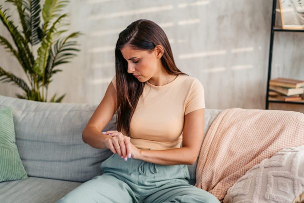 donna seduta sul divano guarda braccio con dermatite