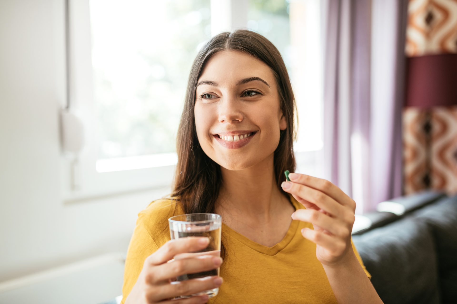 giovane donna sorridente assume integratore alimentare con un bicchiere d'acqua