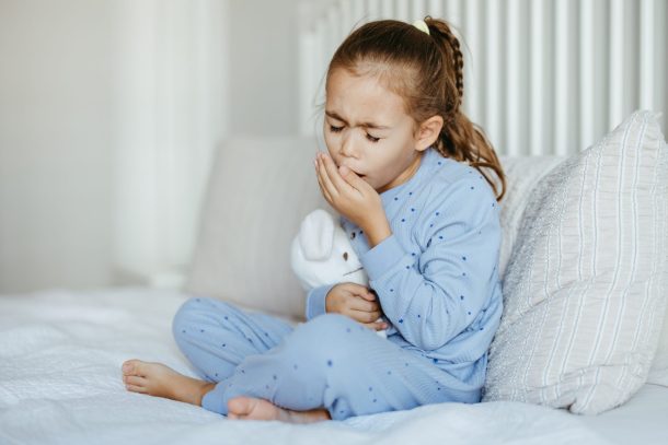 bambina con pigiama celeste seduta sul letto che tossisce