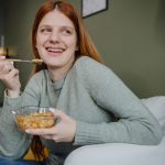 ragazza con capelli rossi sorride mangiando ciotola di legumi