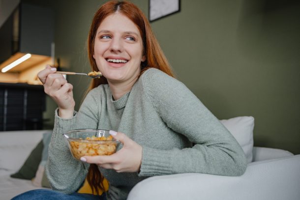 ragazza con capelli rossi sorride mangiando ciotola di legumi
