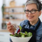 Donna anziana sorridente mangia insalata