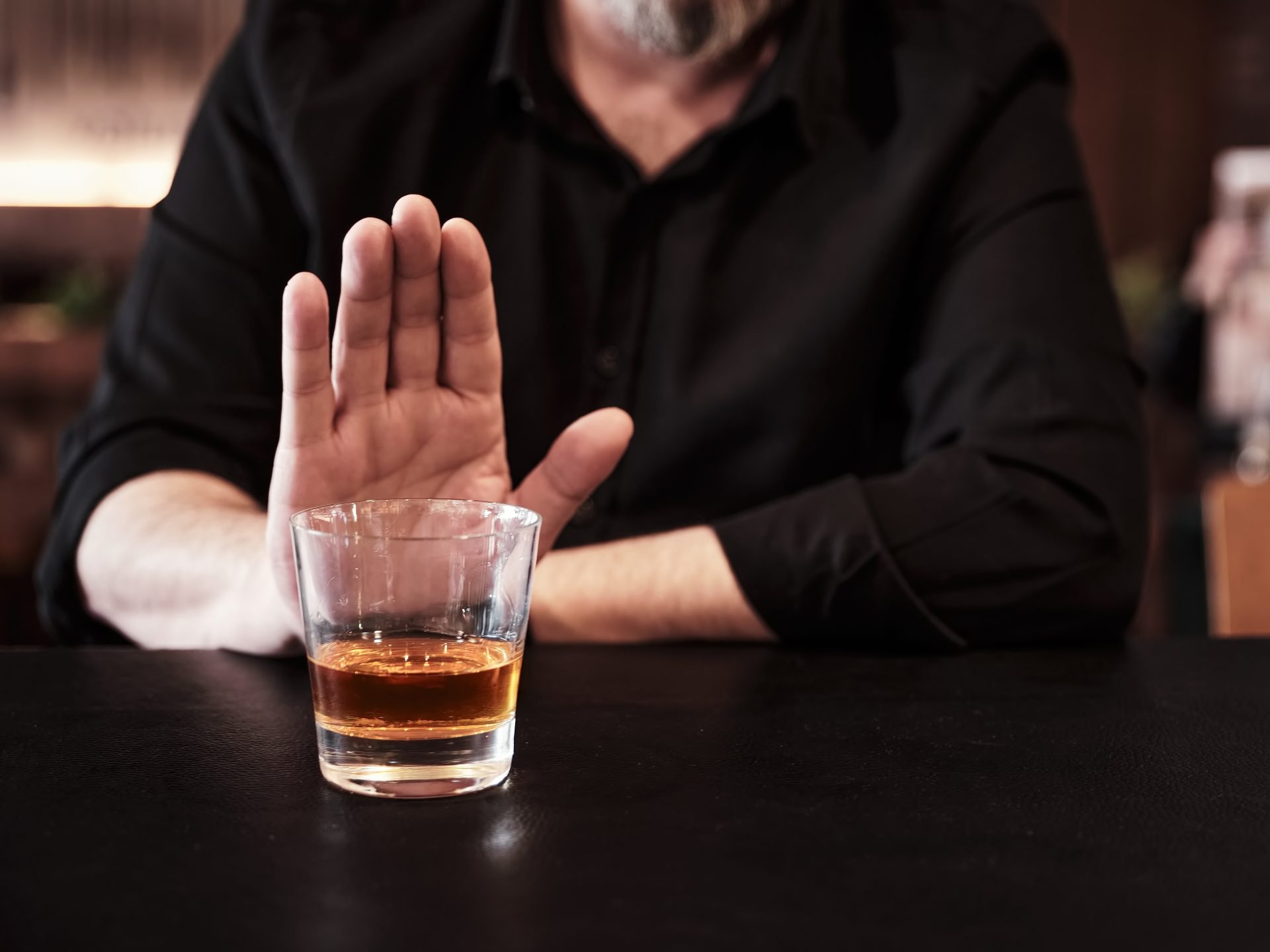 uomo fa gesto di stop davanti a bicchiere di alcol
