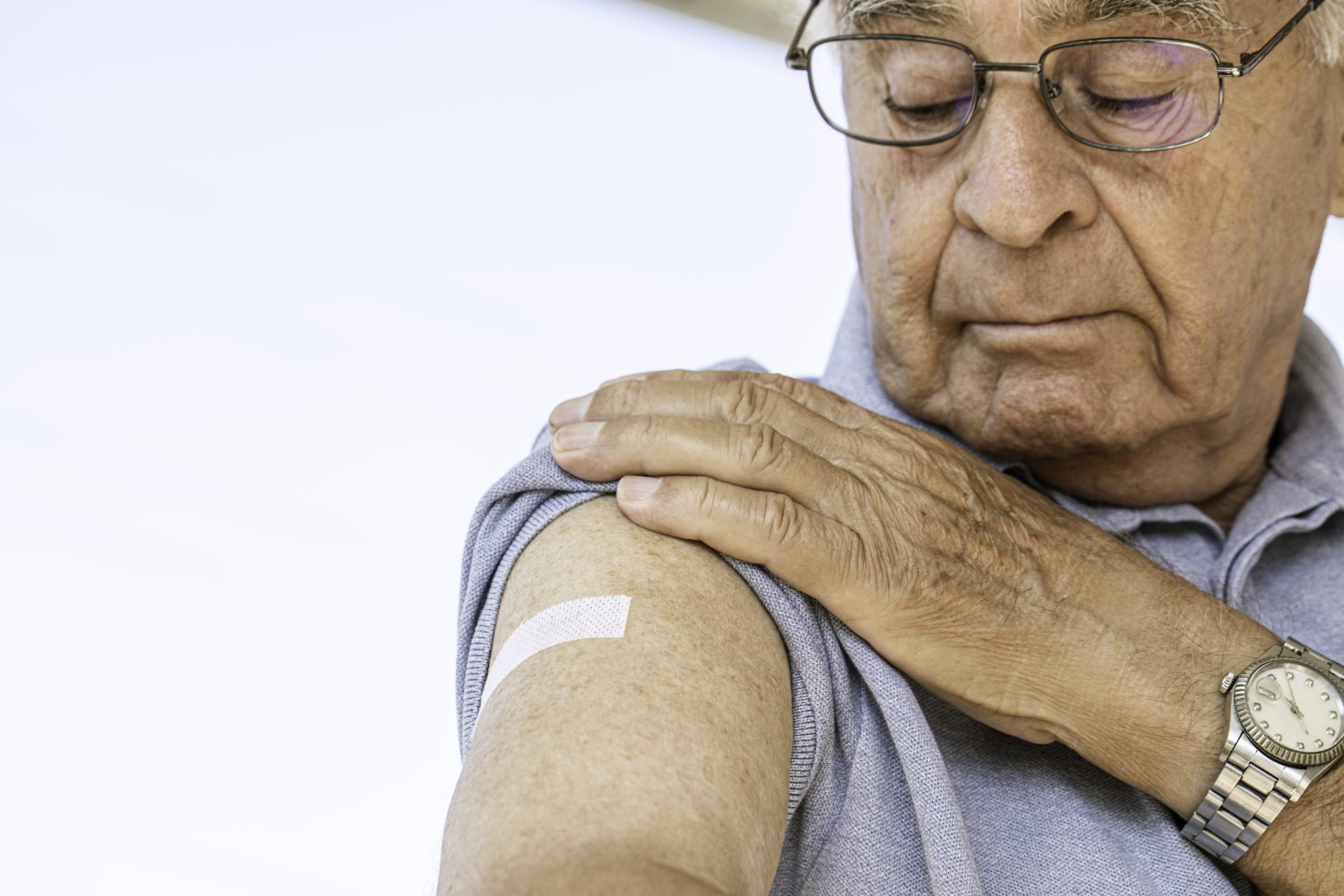 uomo anziano guarda braccio con cerotto dopo vaccinazione