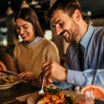 uomo e donna sorridenti mangiano carne