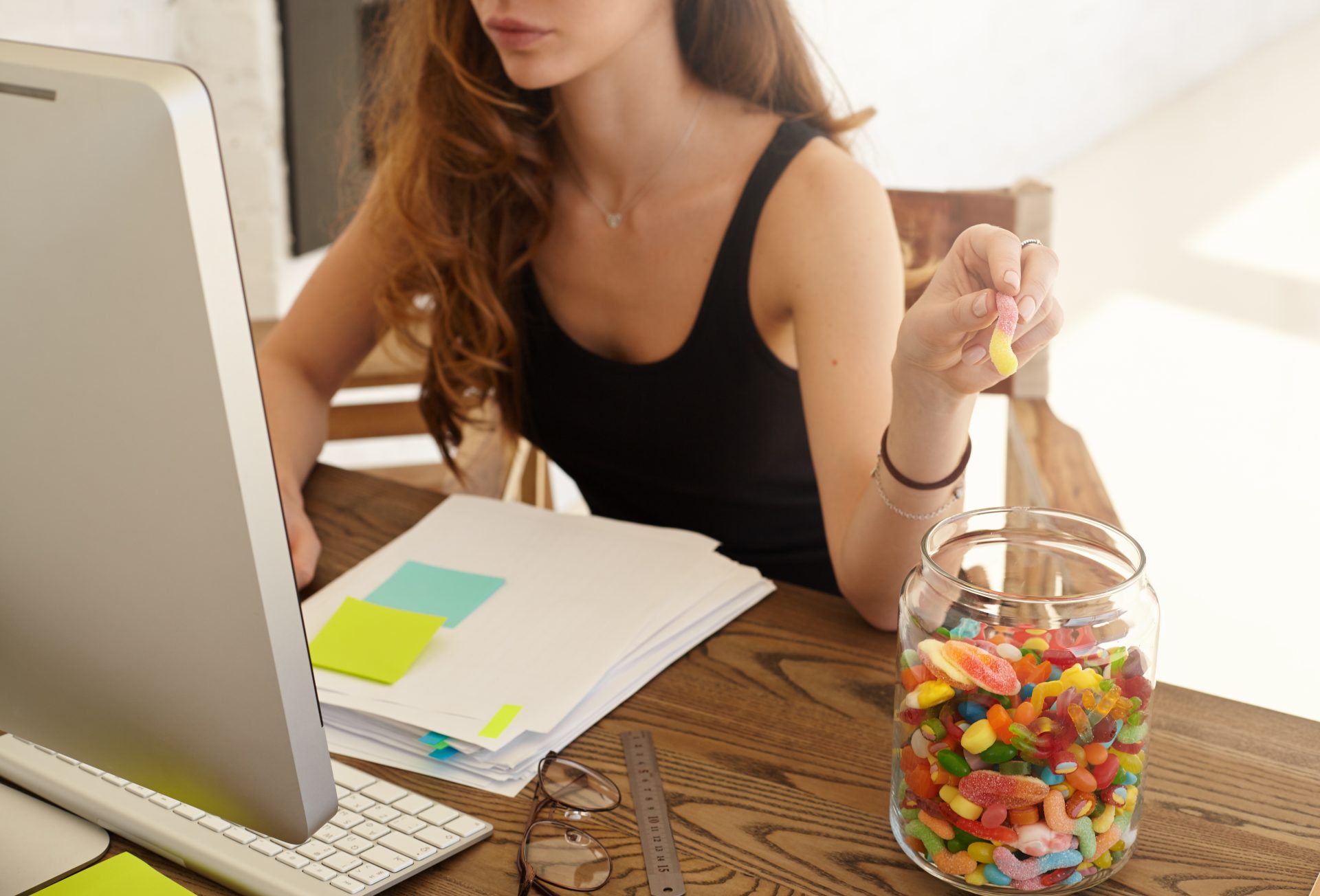 ragazza al computer mangia caramelle da contenitore di vetro