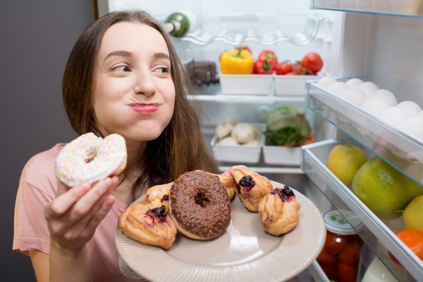 ragazza mangia dolci davanti al frigorifero