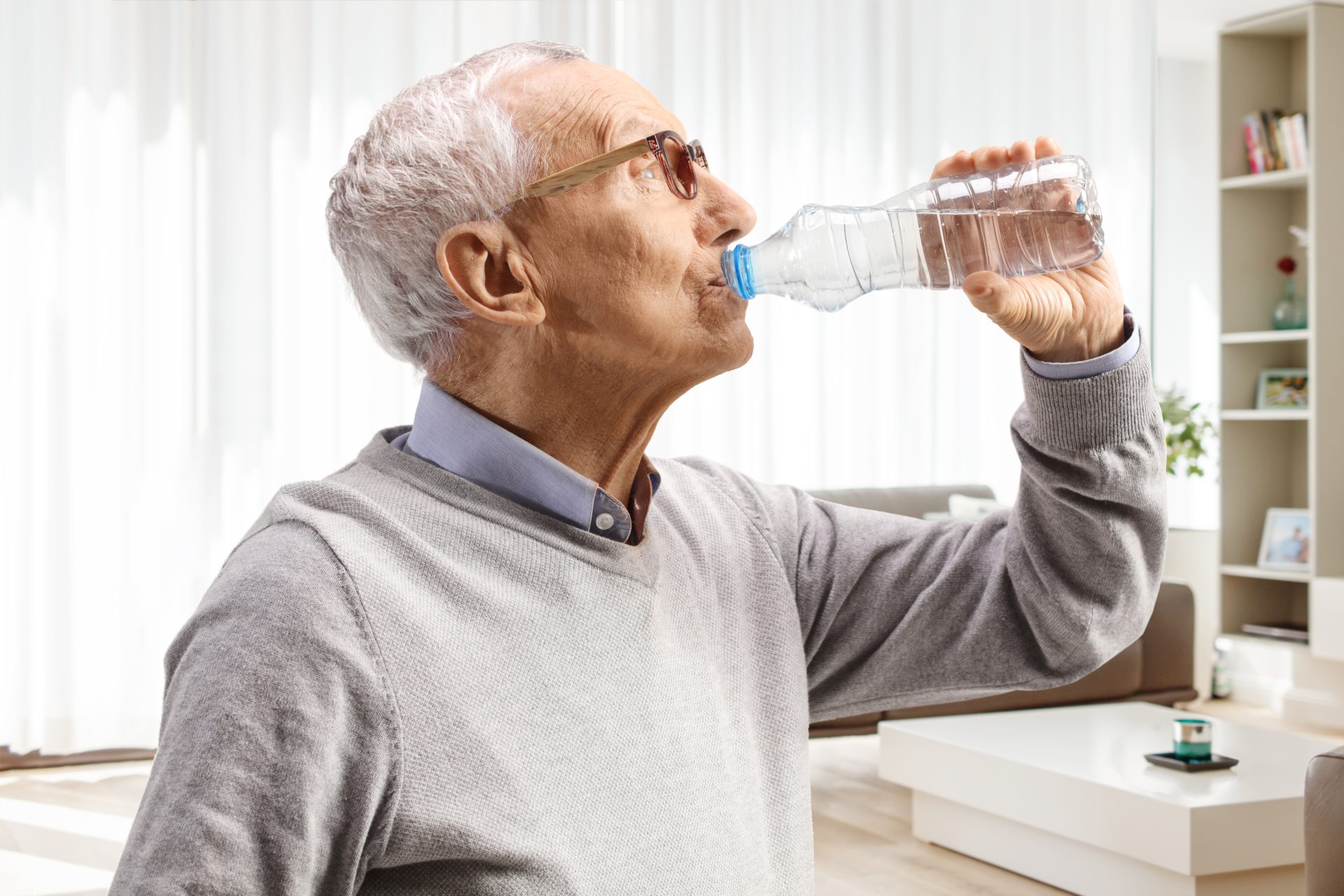 uomo anziano beve da una bottiglia d'acqua