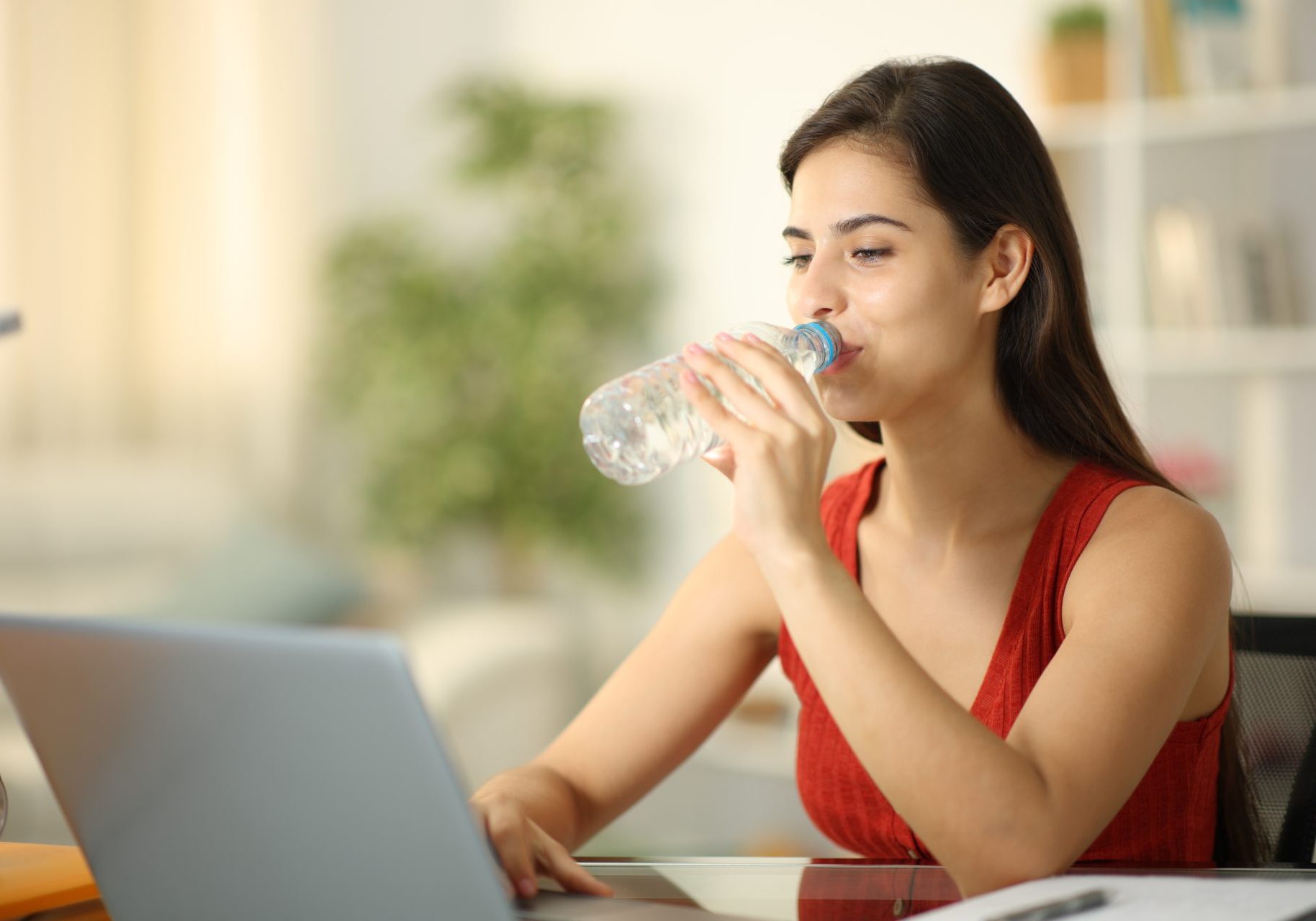 giovane donna davanti al computer beve acqua da bottiglia