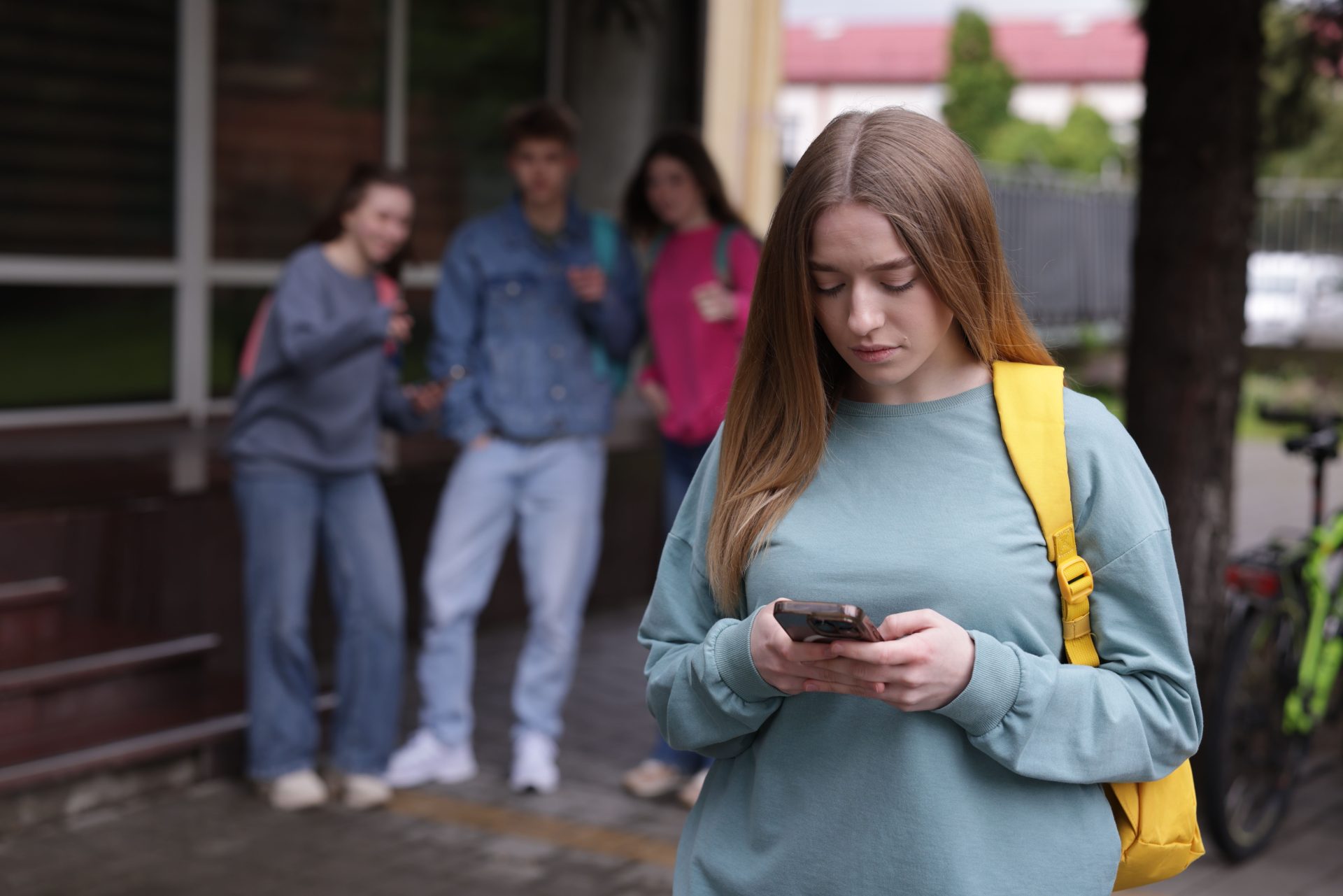 ragazza guarda lo smartphone mentre gruppo di coetanei la osserva sullo sfondo