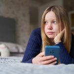 ragazza triste distesa sul letto con il telefono