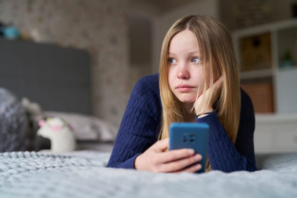ragazza triste distesa sul letto con il telefono