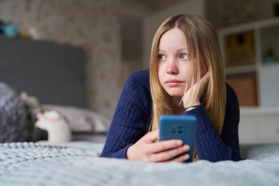 ragazza triste distesa sul letto con il telefono