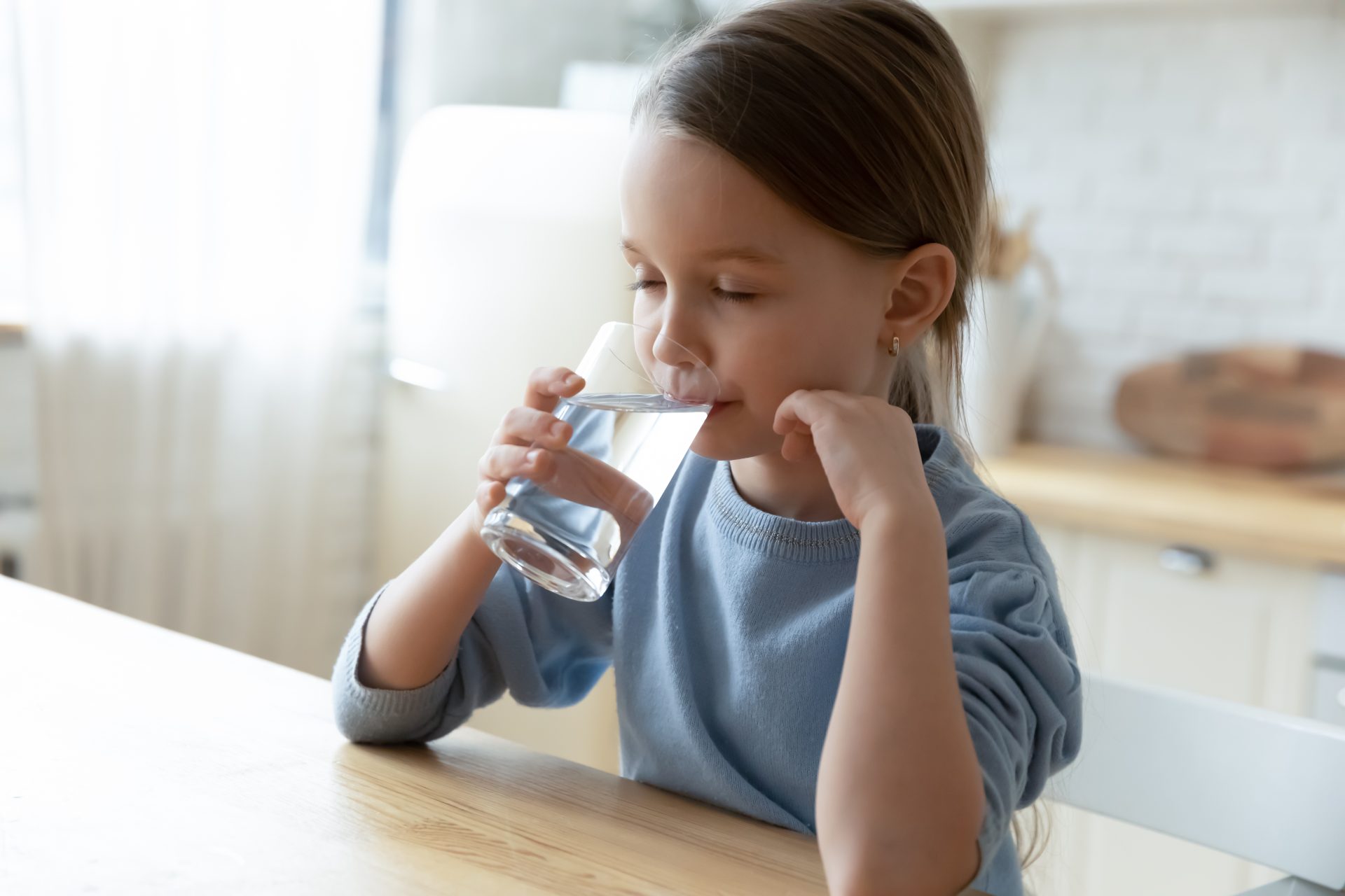 bambina beve acqua al tavolo della cucina