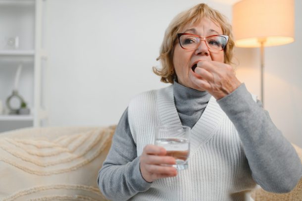 donna anziana prende pillola con bicchiere d'acqua
