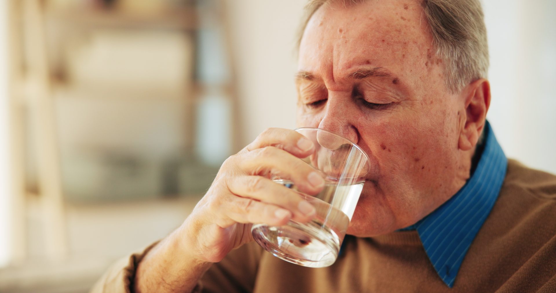 uomo anziano beve bicchiere d'acqua