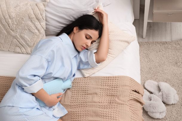 dolori-mestruali-forti_cover giovane donna distesa sul letto con borsa dell'acqua per dolore al ventre