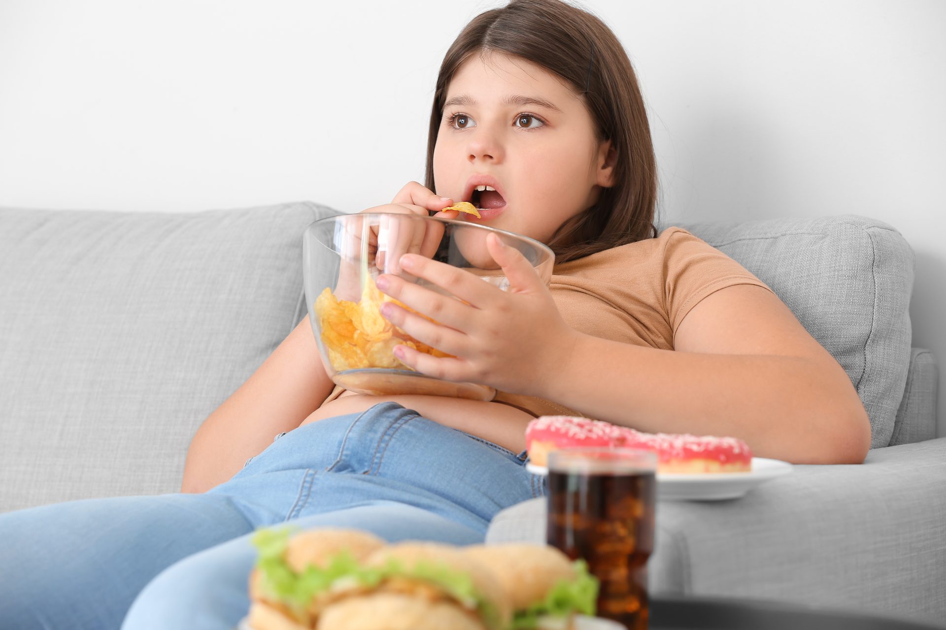 bambina obesa mangia patatine sul divano