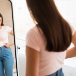 giovane donna frustrata per il proprio aspetto fisico davanti allo specchio