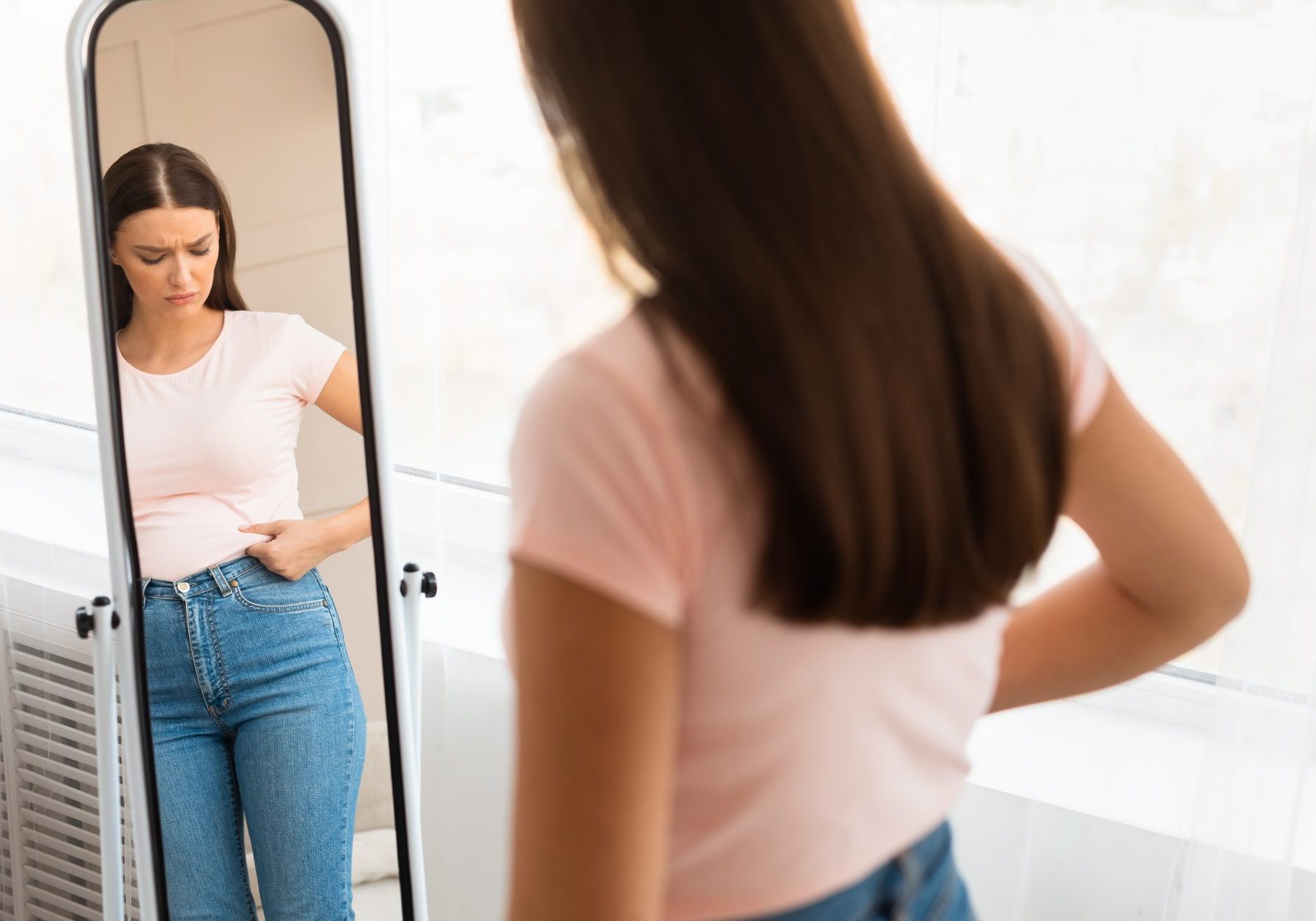 giovane donna frustrata per il proprio aspetto fisico davanti allo specchio