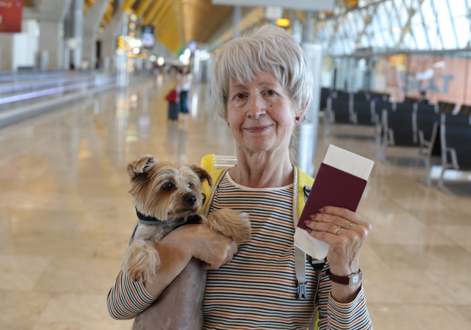 donna anziana con cagnolino in braccio e passaporto in mano