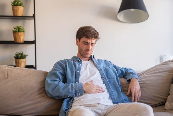 intestino-irritabile_cover giovane uomo seduto sul divano con mal di stomaco