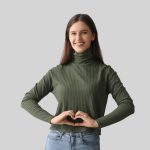 giovane donna sorridente con mani a cuore su addome