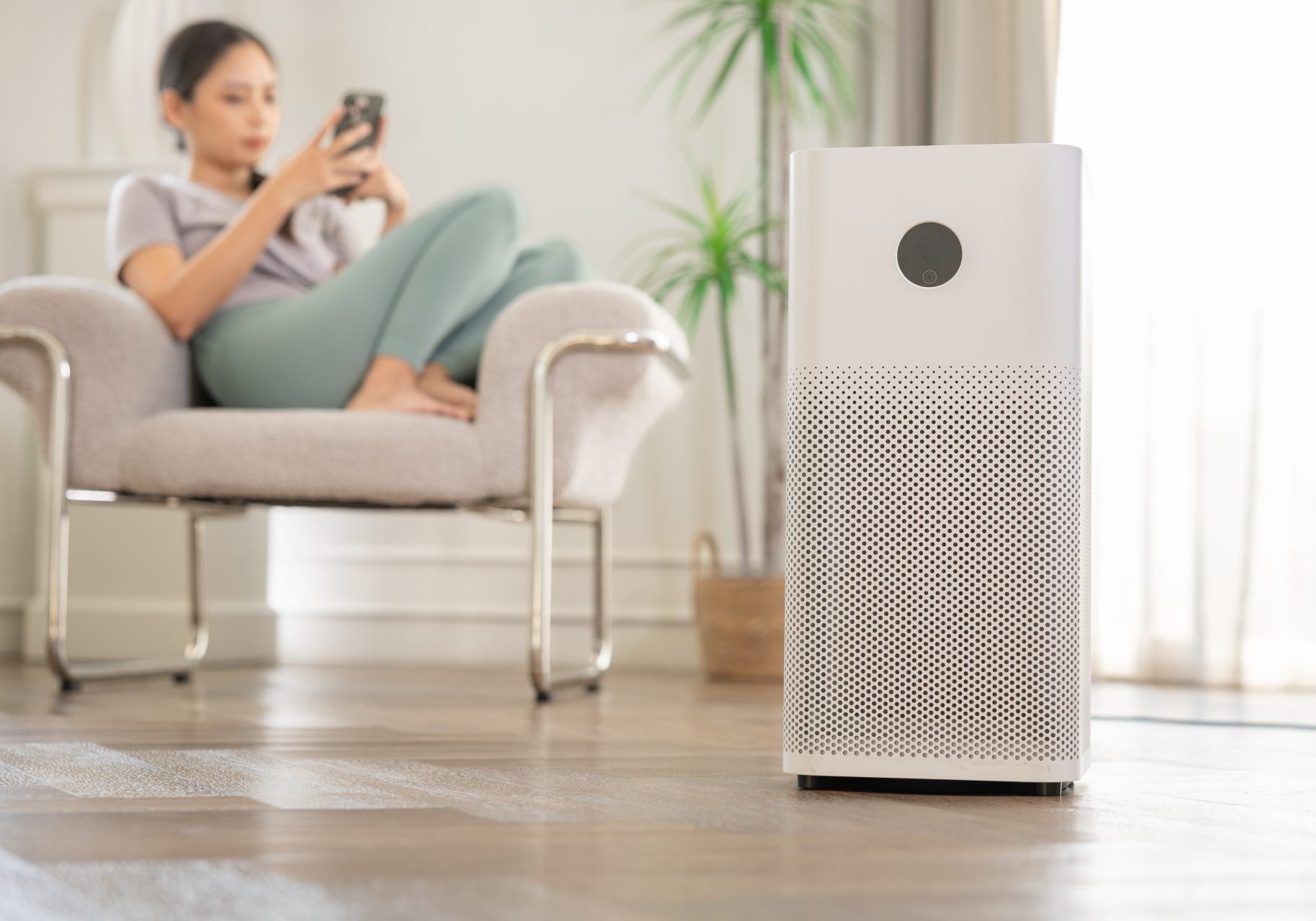 donna usa smartphone su poltrona vicino a purificatore d'aria