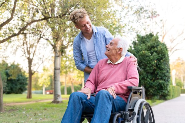 invalidita-permanente_cover caregiver sorride a uomo anziano in sedia a rotelle