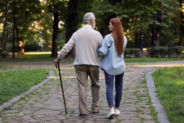anziano-non-autosufficiente giovane donna accompagna anziano con bastone da passeggio
